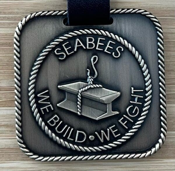 A square metal plaque with the words " seabees we build, we fight ".